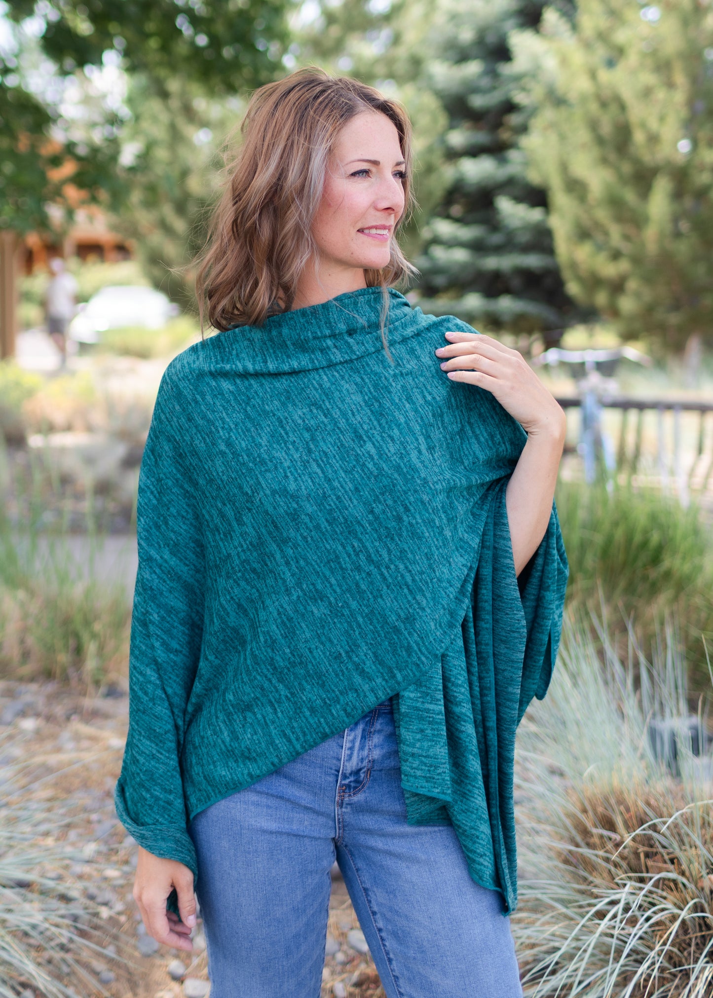 Woman wearing a teal poncho outdoors with trees and grass in the background